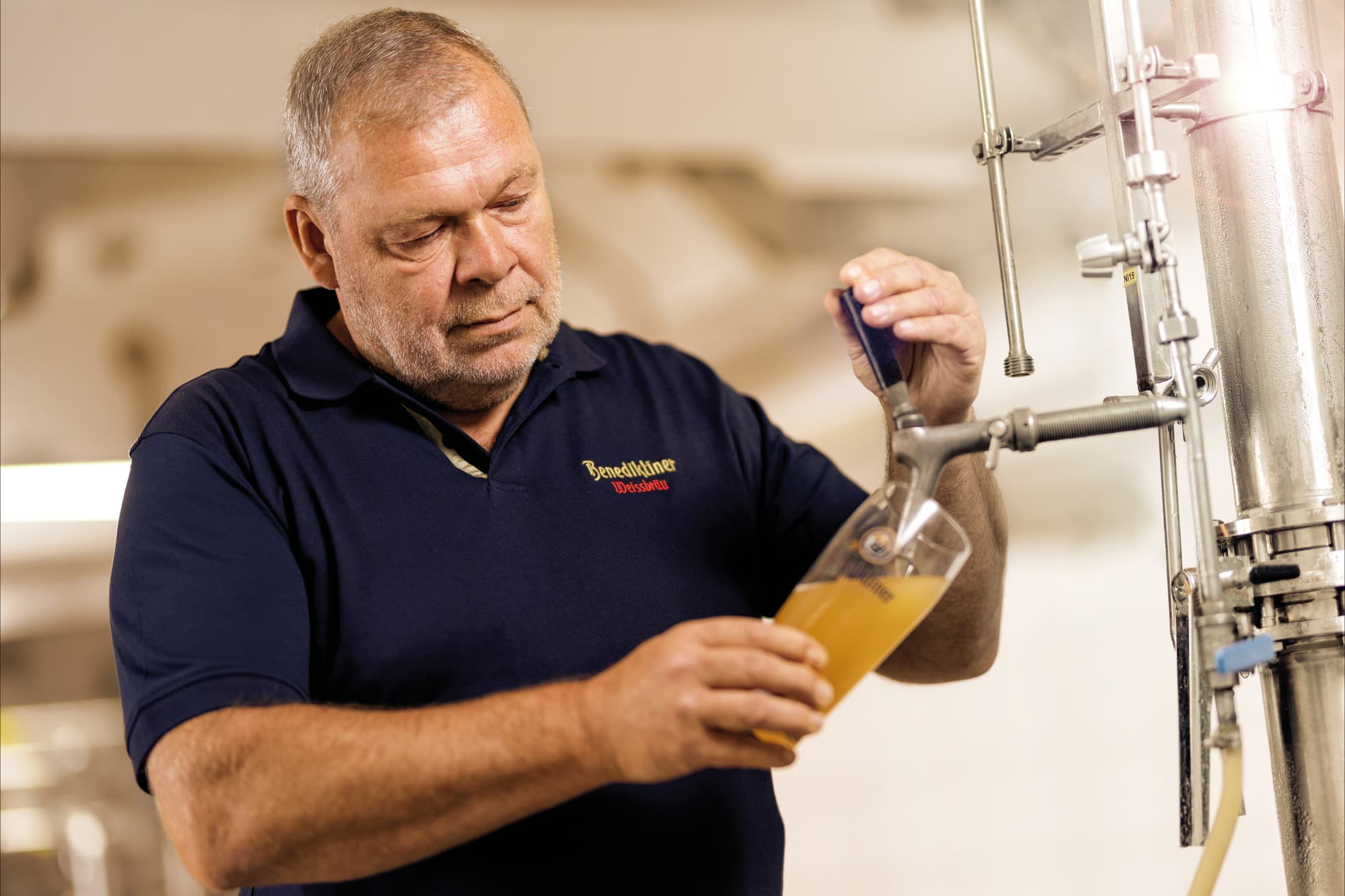 Nhân viên mặc áo Benediktiner Weissbräu rót bia lúa mì đục từ vòi thử ở bồn ủ