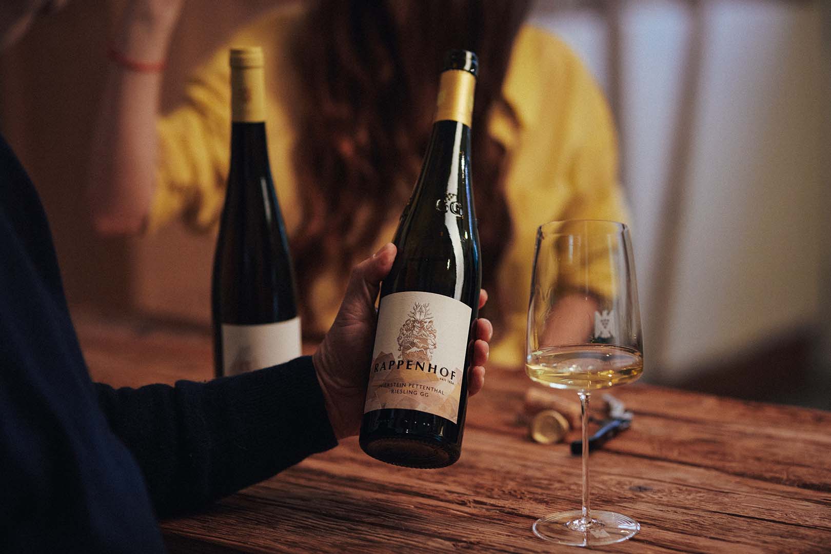 Chai Rappenhof Riesling và ly vang trắng trên bàn gỗ